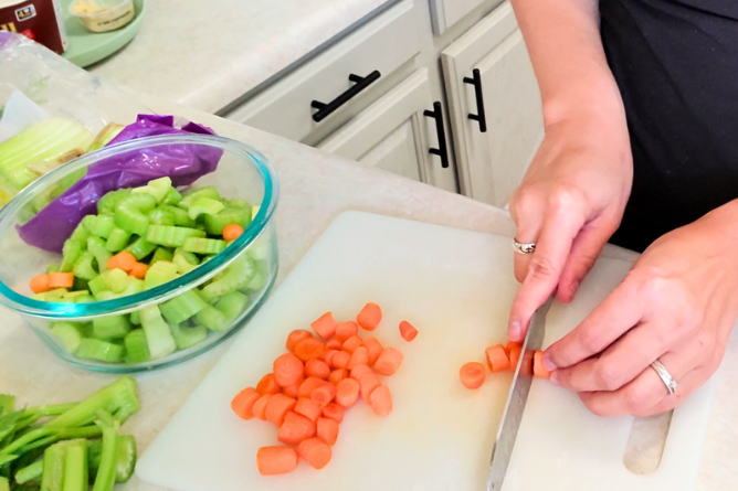Close up of woman cutting carrots next to a bowl of already cut celery