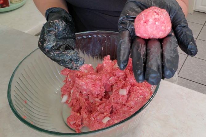 woman holding up a freshly rolled meatball from the bowl of hamburger meat