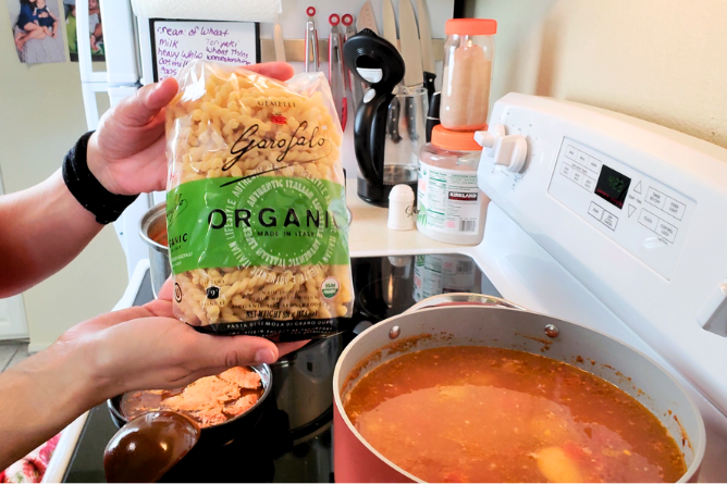 woman holding bad of Garo Falo Organic noodles next to a bowl of soup