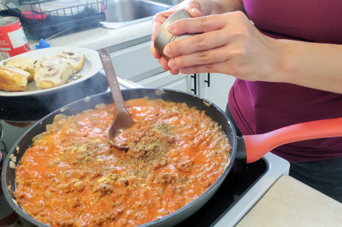 woman pouring Italian seasonings into a homemade pasta sauce