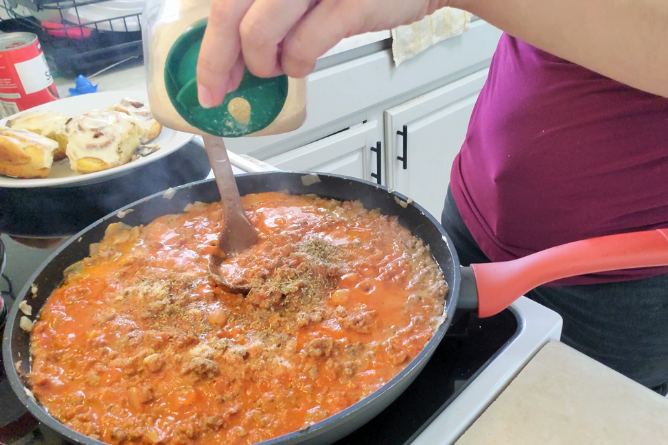 woman about to pour sugar into a homemade pasta sauce