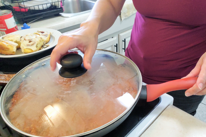 woman covering a large skillet with a lid