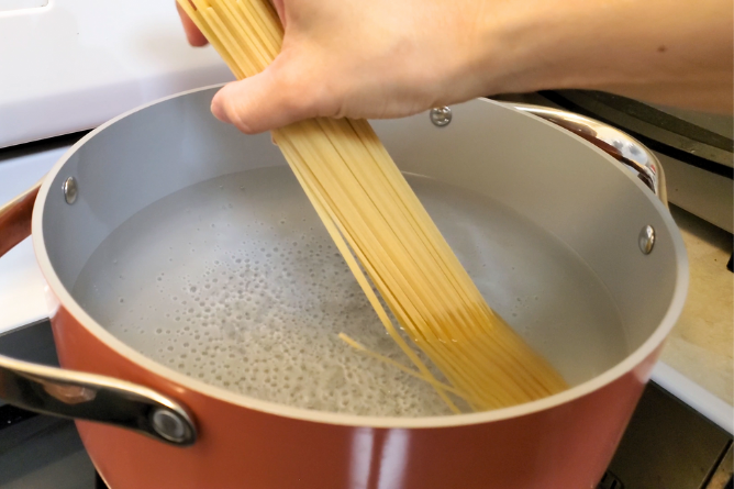 woman placing spaghetti pasta into a large pot of boiling water