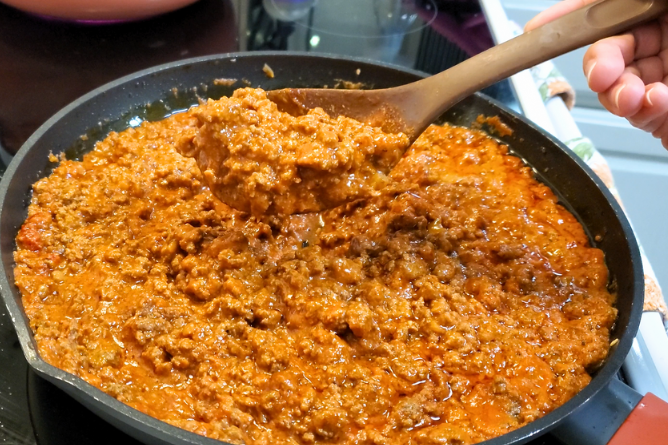 woman holding up a large spoon full of homemade pasta sauce with meat