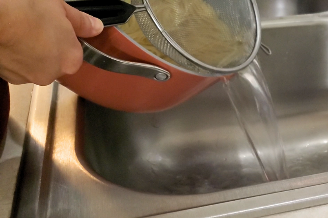 woman draining pasta water from cooked pasta
