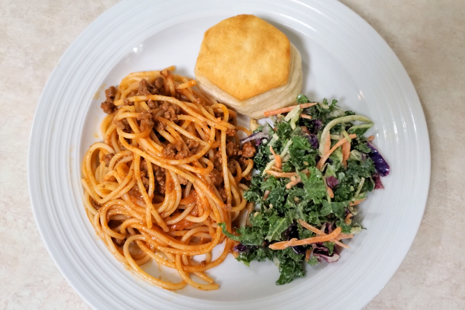 A white plate served with spaghetti, kale salad, and a biscuit