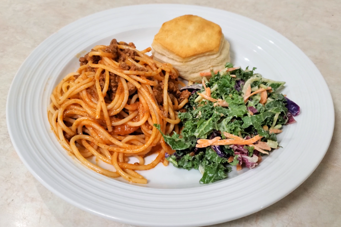 White plate filled with spaghetti, salad, and a biscuit