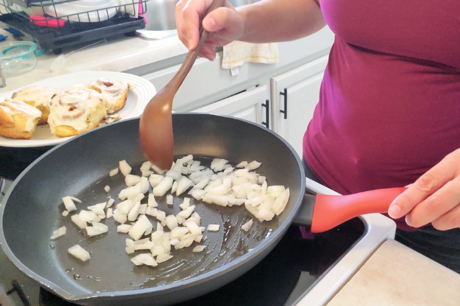 woman stirring hot skillet filled with oil and onions